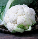 White cauliflower on a wooden surface with green leaves in the background
